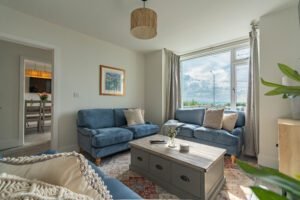 Cozy living room featuring blue sofas, a wooden coffee table, and large windows with views of the outdoors